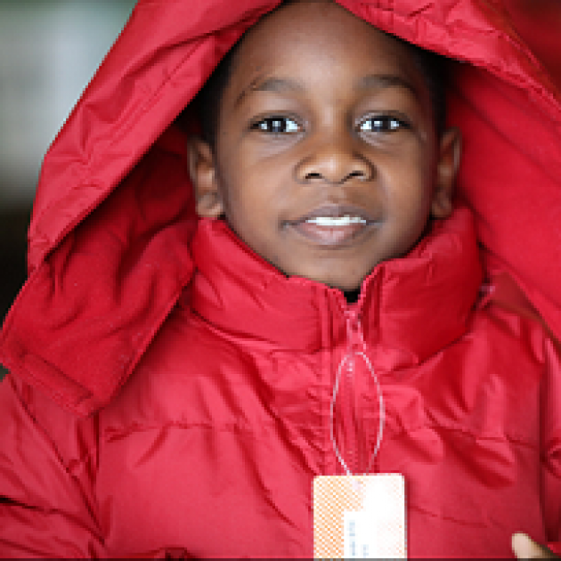Young black child smiling and wearing a red winter coat with a hood