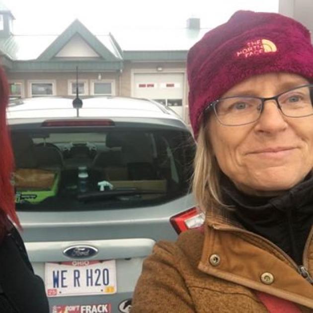 Carolyn on the right, blonde woman with maroon winter hat and glasses standing next to car with Native American woman on right