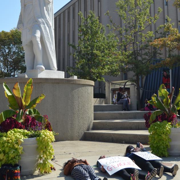 Student lying on ground beneath Columbus statue