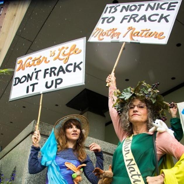 Two women dressed in gowns with protest signs saying Don't Frack it up and It's not nice to frack mother nature