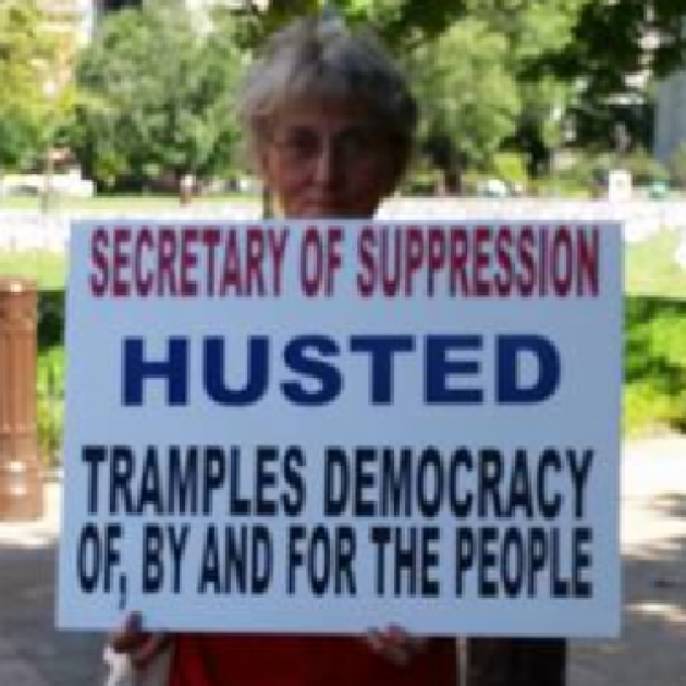 Woman holding sign against Jon Husted