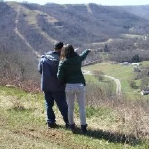 Backs of two people standing outside on a hill pointing off to the distance down in a valley