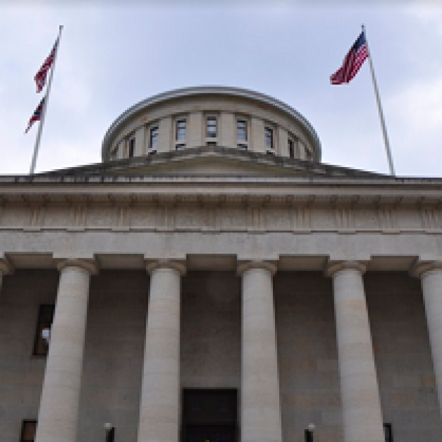 Big white government building with columns and a round top and  flags flying on each side