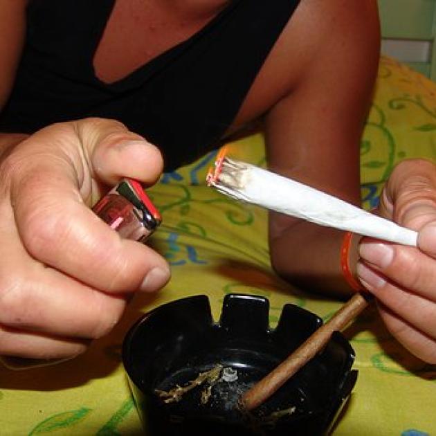 Person's hands lighting a huge joint over an ashtray