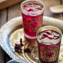 Two glasses with gold designs on the outside and red liquid inside on a pretty gold flouted tray against a wooden tabletop