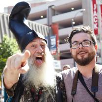 Guy with white beard and funny hat standing next to young man with glasses