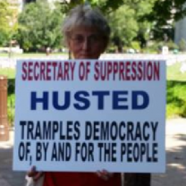 Woman holding sign against Jon Husted
