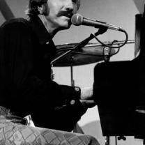 Black and white photo of guy with big mustache sitting at piano singing