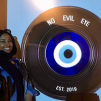 Black woman standing next to a large film reel that says No Evil Eye on it