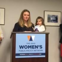 Woman holding a baby at a podium that says Women's Public Policy Network