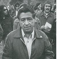 Black and white photo of Latino man wearing a jacket outside in front of a lot of other people