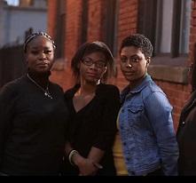 Three black women standing outside a brick building