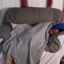 Young black woman asleep under huge blanket on a gray loveseat