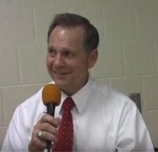 White man with brown hair, white shirt and red tie talking into a microphone