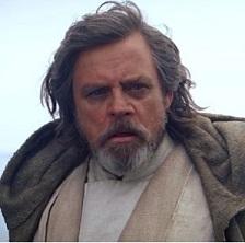 Older man with unkempt gray long hair and a beard looking intensely at the camera wearing a cape