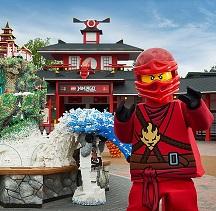 Robot looking character in red suit and helmet standing by and in front of structures made out of legos
