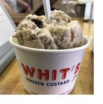Round carton container with words Whit's in red on white with goopy brownish concoction inside like ice cream and a spoon sticking out the top