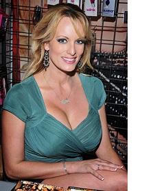 White woman with long blonde hair and large breasts with lots of cleavage in a green dress smiling