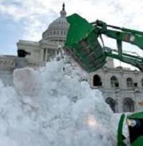 Big white stately building with round top and lots of windows behind a huge green truck with a big arm and huge shovel putting a ton of white snow in a big pile in front