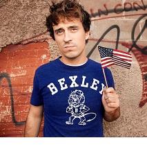 Young white man with brown hair and a Bexley T-shirt holding a small American flag