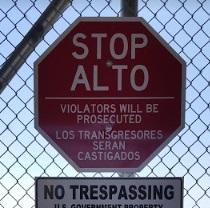 Stop sign in Spanish on a wire fence and sign that says No Trespassing