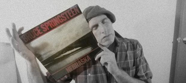 Guy wearing a beret with his eyes closed holding an album cover of Springsteen's Nebraska up to his face