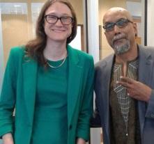Tall thin white woman smiling with glasses and a green dress next to an older black man in a suit making a peace sign