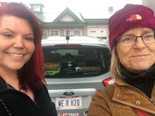 Carolyn on the right, blonde woman with maroon winter hat and glasses standing next to car with Native American woman on right