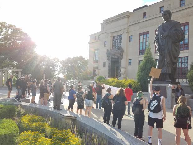 People protesting outside City Hall and large Columbus statue