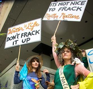 Two women dressed in gowns with protest signs saying Don't Frack it up and It's not nice to frack mother nature