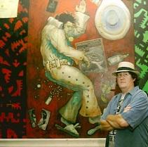 White man in blue shirt with straw hat with arms folded standing in front of huge mural of Elvis Presley
