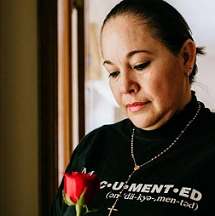 Latina woman looking down at a red rose in our hand