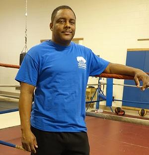 Black man in blue t-shirt standing next to a boxing ring
