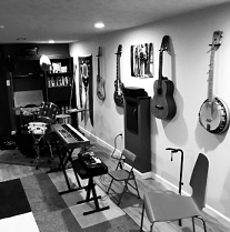 Black and white photo of room with lots of guitars and a banjo hanging on the wall and other musical instruments