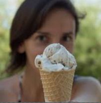 Young white girl with brown hair holding an ice cream cone in front of her face