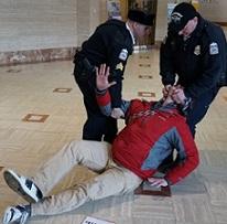 Man being dragged across the floor by two uniformed policemen