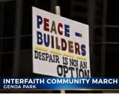 Words on a picket sign Peace Builders Despair is not an option and the banner lower third below saying Interfaith Community March, Genoa Park