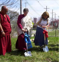 Three people digging into the ground, two wearing Buddhist garb