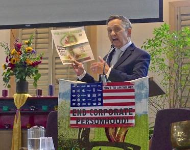 Dennis Kucinich, 60-ish white guy in a suit at a podium holding up a copy of the Free Press