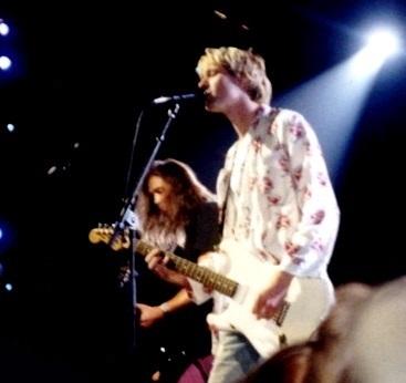 Kurt Cobain singing into a mic and a guitarist behind him