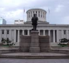 Large black statue of a man on a pedestal in front of a large white government building with many columns