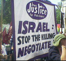 People protesting outside with sign saying Israel stop the killing, negotiate