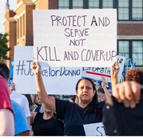 Woman outside holding a sign that says Protect and Serve not Kill and Coverup