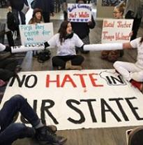 People sitting around a huge banner saying No Hate in our State