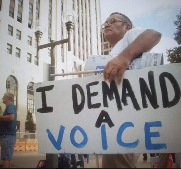 Man holding sign saying I Demand A Voice