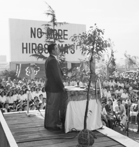 Guy at a platform speaking to a crowd with sign No More Hiroshimas