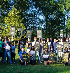 People posing outside by trees with signs