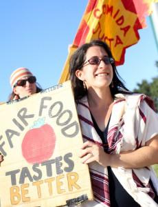 White women with long dark hair and sunglasses holding sun that says Fair Food Taste Better