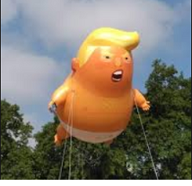 Big inflated balloon shaped like a fat baby in a diaper with orange skin and large yellow hair flowing at the top with his mouth open held up high in the air by strings