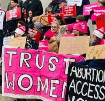 People at a rally holding signs saying Abortion Access and Trust Women